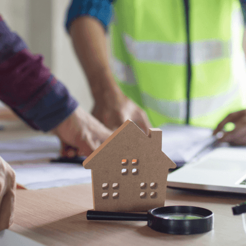 Services 1 Wooden house cut-out and magnifying glass on building plans while surveyors review drawings